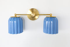 Double Marcella Sconce by Sazerac Stitches featuring two sky blue glazed ceramic shades with a ridged Art Deco silhouette, paired with warm brass hardware. Handmade in the USA, this feminine yet bold ceramic wall light works beautifully above a bathroom vanity, in a hallway, or flanking a bed for a colorful and timeless design statement.