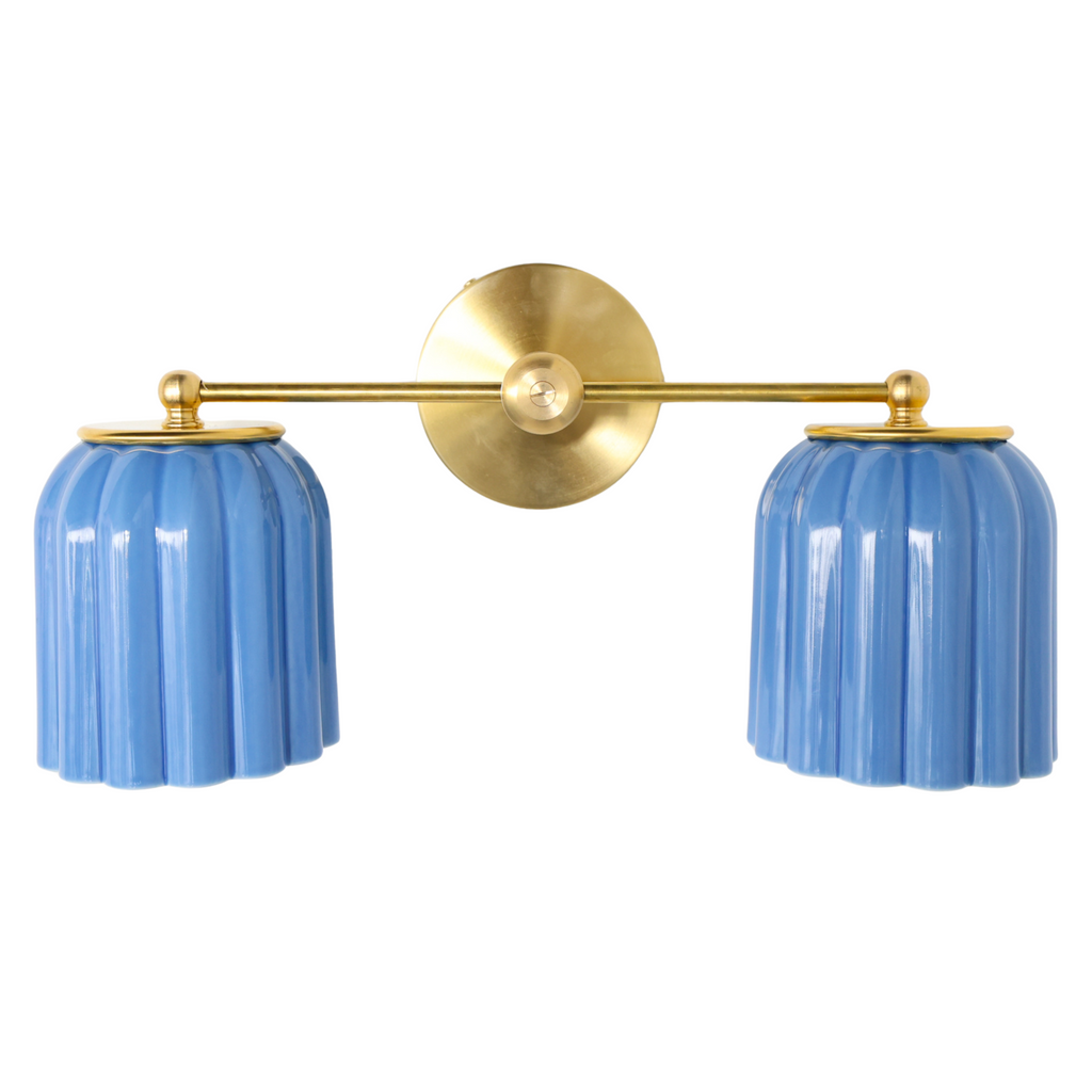 Double Marcella Sconce by Sazerac Stitches featuring two sky blue glazed ceramic shades with a ridged Art Deco silhouette, paired with warm brass hardware. Handmade in the USA, this feminine yet bold ceramic wall light works beautifully above a bathroom vanity, in a hallway, or flanking a bed for a colorful and timeless design statement.