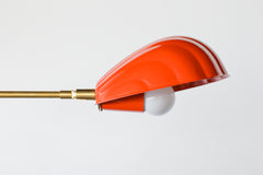 The Coquille Chandelier in Flame is a bold, sculptural light fixture featuring three scallop shell-shaped shades in a vibrant red-orange powder-coated finish. Suspended from a central brass rod, each shell houses a globe bulb and radiates from a sleek brass frame, combining coastal lighting style with vintage Art Deco influence. This modern chandelier is handcrafted for statement interiors and is perfect for dining rooms, bedrooms, or eclectic spaces seeking designer lighting with color and personality.