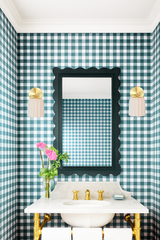 Traditional powder room with Southern charm featuring green gingham wallpaper, cream ceramic Marcella wall sconces with brass backplates, a scalloped black mirror, and a classic white marble vanity with brass fixtures. The fluted sconces and playful patterns give the space a timeless yet updated feel, perfect for a preppy, coastal-inspired home in Nantucket or a refined Southern cottage.