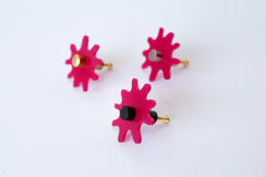 Close-up view of a single Splat drawer pull in hot pink acrylic with a brass detail, highlighting its splat-shaped design and high-quality materials.