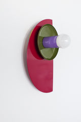 This sculptural Kin Sconce features a dynamic mix of deep black cherry red, earthy olive, and soft orchid purple. The high-gloss finish adds dimensionality to its clean, graphic form—half-circle, cone, and disc layered together in an artful composition. Ideal for modern, postmodern, or maximalist spaces in need of a functional focal point.