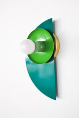 A sculptural Kin Sconce in a tone-on-tone palette of Mermaid Green, Spring Green, & Vista Green, mounted on a clean white wall. The spring green shade and pastel green socket cup sit against a glossy half-moon backplate in vibrant Mermaid Green, creating a layered, Bauhaus-inspired silhouette. The rich monochromatic color scheme gives this geometric fixture a bold, modern presence that works beautifully in eclectic interiors or maximalist spaces.