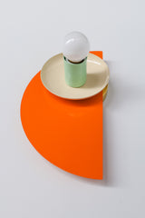 Vibrant modern light fixture with overlapping steel shapes in orange, cream, and mint green, styled with a G16.5 white globe bulb. The Kin Sconce adds a retro-futuristic pop of color and design to contemporary or eclectic interiors.