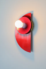 Angled wall-mounted view of the Kin Sconce in a bright red, plum, and blue color-block palette, showing off its layered geometric design.