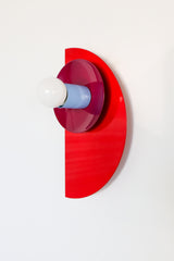 Angled wall-mounted view of the Kin Sconce in a bright red, plum, and blue color-block palette, showing off its layered geometric design.