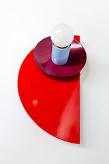 Angled wall-mounted view of the Kin Sconce in a bright red, plum, and blue color-block palette, showing off its layered geometric design.