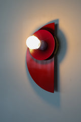 Angled wall-mounted view of the Kin Sconce in a bright red, plum, and blue color-block palette, showing off its layered geometric design.