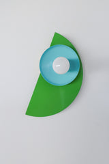 Close-up of the Kin Sconce in a color-blocked palette of bright green, turquoise, and sky blue, topped with a round white bulb.