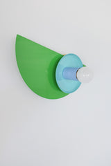 Close-up of the Kin Sconce in a color-blocked palette of bright green, turquoise, and sky blue, topped with a round white bulb.