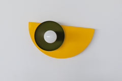 Colorful Kin wall sconce featuring a glossy yellow powder-coated backplate, olive green dish, and terra cotta socket, photographed against a white wall—ideal for maximalist, eclectic, or midcentury modern interiors seeking a pop of color and playful geometric wall lighting.