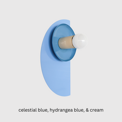 Color-drenched Kin Sconce in celestial blue and hydrangea with a cream socket and brass backplate, ideal for monochromatic bedroom wall lighting or bold hallway installations. A perfect fit for eclectic design lovers seeking playful, sculptural lighting with a modern silhouette and saturated color palette.