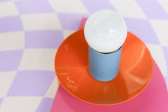 An eye-catching Kin Sconce in a vibrant trio of doll pink, orange peel, and hydrangea blue, set against a whimsical lavender and white warped checkerboard background. The glossy finishes and saturated hues lend a retro-modern energy that works beautifully in Memphis, postmodern, or colorful maximalist spaces. This wall light functions as both a statement piece and functional lighting for bedrooms, bathrooms, or studio nooks.