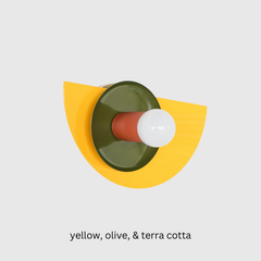 Colorful Kin wall sconce featuring a glossy yellow powder-coated backplate, olive green dish, and terra cotta socket, photographed against a white wall—ideal for maximalist, eclectic, or midcentury modern interiors seeking a pop of color and playful geometric wall lighting.