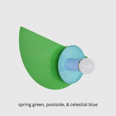 Close-up of the Kin Sconce in a color-blocked palette of bright green, turquoise, and sky blue, topped with a round white bulb.