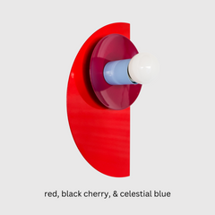 Bauhaus-inspired Kin Sconce featuring a powder-coated red base, black cherry reflector disc, and celestial blue socket cup.  A sculptural, geometric wall light that adds a punch of color and modern edge to bathrooms, hallways, or playful minimalist interiors.