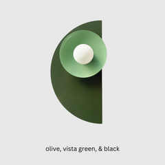 The Kin Sconce in a moody mix of olive green, vista green, and black, featuring layered geometric shapes and a round white bulb. A bold, sculptural wall fixture that blends Bauhaus formality with Memphis-inspired color blocking—perfect for interiors that lean modern, eclectic, retro, or maximalist. Works beautifully in creative offices, powder rooms, or as a statement-making hallway sconce.
