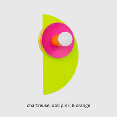 The neon Kin Sconce in chartreuse, doll pink, and orange, featuring a sculptural half-circle backplate and circular shade with a central bulb. This wall sconce channels bold Memphis Group energy with Bauhaus-inspired geometry and saturated color blocking—perfect for playful interiors, maximalist spaces, kids' rooms, or modern art-forward homes that embrace high-impact, unconventional design.