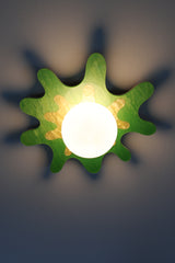 Green and yellow splatter-shaped wall sconce with a frosted globe, casting playful shadows on the wall.