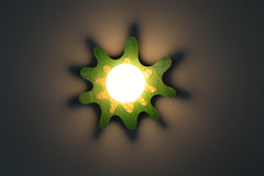 Green and yellow splatter-shaped wall sconce with a frosted globe, casting playful shadows on the wall.