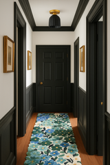 Black ceramic flushmount ceiling light with sculptural fluted detailing and a warm brass canopy, installed in a bold black-and-white hallway. The handmade light fixture features an Art Deco silhouette that pairs beautifully with the high-contrast trim and wainscoting. A colorful floral hallway runner in shades of teal, blue, and green adds a cheerful pop to the space, balancing the moody architectural elements. Ideal for interior design lovers seeking unique, modern lighting with vintage style influence.