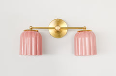 Front-facing product image of the Double Marcella Sconce in pastel pink ceramic with brass hardware, handmade by Sazerac Stitches. The glossy ridged shades highlight a playful yet timeless Art Deco design, ideal for use above a vanity, in a hallway, or as a bold accent in a bedroom or entryway.