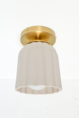 Close-up of the Marcella Flushmount ceiling light with an unglazed porcelain ceramic shade and brass canopy. This handmade flush mount features Art Deco-inspired fluted curves and sculptural detailing, perfect for bathrooms, hallways, and elegant low-ceiling spaces. The soft white finish adds a timeless, neutral look ideal for minimal and maximalist interiors alike.