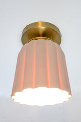 Close-up of the Marcella Flushmount ceiling light with an unglazed porcelain ceramic shade and brass canopy. This handmade flush mount features Art Deco-inspired fluted curves and sculptural detailing, perfect for bathrooms, hallways, and elegant low-ceiling spaces. The soft white finish adds a timeless, neutral look ideal for minimal and maximalist interiors alike.