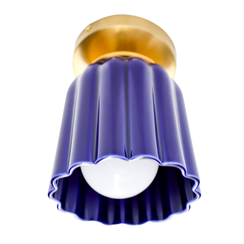 Marcella flushmount light fixture in glazed cobalt blue ceramic with a fluted Art Deco-inspired shape and warm brass canopy. A sculptural, handmade ceiling light perfect for hallways, powder rooms, or color-drenched interiors. Elegant blue ceramic flush mount with vintage charm.