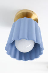 Detail view of the handmade Marcella ceramic flush mount light in unglazed soft blue with scalloped edges and brass hardware. A sculptural Art Deco ceiling light fixture perfect for colorful interiors, hallways, and small spaces.