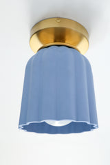 Detail view of the handmade Marcella ceramic flush mount light in unglazed soft blue with scalloped edges and brass hardware. A sculptural Art Deco ceiling light fixture perfect for colorful interiors, hallways, and small spaces.
