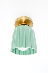 Jade green ceramic flush mount ceiling light with fluted Art Deco silhouette and brass canopy. Handmade sculptural lighting fixture designed for bathrooms, hallways, or entryways. Modern pastel green ceiling light adds a pop of color and vintage-inspired charm to interiors.