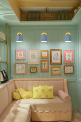 Three unglazed soft blue and brass Marcella sconces mounted above a playful gallery wall in a pastel-hued built-in seating nook; the fluted ceramic fixtures complement the room’s candy-colored palette and scalloped millwork, perfect for eclectic, maximalist, or whimsical interiors with vintage, cottagecore, or southern charm influences.