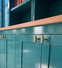 Customer-installed Milne Knobs in solid brass shown on vibrant teal painted cabinetry with oak countertop. The three-piece curvy brass cabinet knobs add a bold yet refined detail to the custom cabinetry, blending classic craftsmanship with a modern pop of color. This stylish hardware choice elevates the eclectic, maximalist look of the space while offering functionality and visual interest. Ideal for kitchens, built-ins, or statement storage units, the Milne Knob is available in all brass or a mixed brass a
