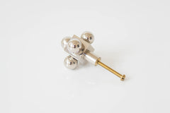 A close-up of a modern cabinet knob with a sculptural design featuring polished nickel spheres and a brass screw base.