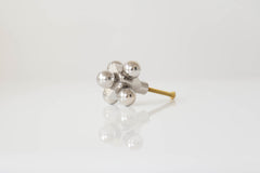 A close-up of a modern cabinet knob with a sculptural design featuring polished nickel spheres and a brass screw base.