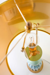 Overhead detail of the Mint & Ceramic Aqua Lamp showing polished brass hardware, filament bulb, and the reflective gold interior of the drum lampshade. Highlights premium craftsmanship and luxurious mid-century style finishes.