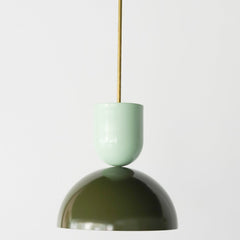 Close-up of the Taeuber Pendant in olive green and mint by Sazerac Stitches, featuring a sleek, two-tone powder-coated steel finish with a brass downrod. The pendant’s sculptural, midcentury-inspired shape highlights the contrast between soft pastel mint and deep olive, creating a sophisticated yet playful color pairing. Handcrafted in the U.S., this modern pendant light is ideal for kitchens, dining areas, and colorful interiors seeking bold design and artisan craftsmanship.