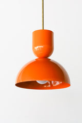 Close-up of the Taeuber Pendant in bright orange by Sazerac Stitches, showcasing its sculptural double-dome silhouette and glossy powder-coated finish with a brass downrod. This modern, handmade pendant light highlights the bold color and smooth craftsmanship of the design, perfect for kitchens, dining nooks, and modern interiors seeking a pop of color and midcentury-inspired style.