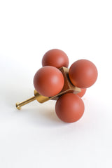 A sculptural oversized drawer pull made with five smooth, matte terra cotta-colored resin spheres arranged around a solid brass cube core. This bold and modern cabinet knob is designed to make a statement, adding an artistic and architectural touch to any dresser, credenza, or built-in cabinetry. Shown on a clean white background to highlight its form and contrast in texture and material.