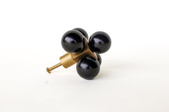 An oversized decorative drawer pull featuring five glossy black spheres arranged around a solid brass cube. The cube is mounted to a brushed brass stem and screw, designed for installation on cabinets or drawers. The geometric design and mixed materials give it a sculptural, modern look with a midcentury flair. Photographed on a clean white background.