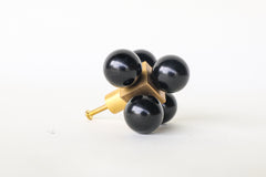 An oversized decorative drawer pull featuring five glossy black spheres arranged around a solid brass cube. The cube is mounted to a brushed brass stem and screw, designed for installation on cabinets or drawers. The geometric design and mixed materials give it a sculptural, modern look with a midcentury flair. Photographed on a clean white background.