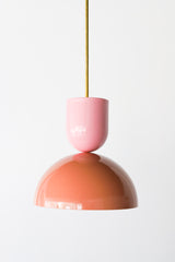 Close-up of the Taeuber Pendant in pastel pink and peach by Sazerac Stitches, featuring a glossy two-tone powder-coated finish and brass downrod. This sculptural pendant light showcases minimalist curves and handcrafted detailing, blending midcentury modern design with a soft, neutral palette. Perfect for kitchens, dining rooms, or entryways, this artisan-made fixture adds a timeless and elegant touch to both contemporary and classic interiors.