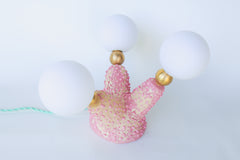 Close-up of the glossy, bumpy, bubblegum-pink glaze on this one-of-a-kind sculptural ceramic lamp, highlighting the hand-built texture, pastel pink underglaze, and 1-inch raw brass spheres that connect to glowing G9 bulbs—perfect for fans of offbeat, creature-inspired home accents and modern handmade lighting.