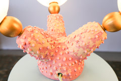 Pink sculptural creature lamp glowing in moody lighting, featuring hand-built ceramic tentacles and glowing white glass globes for unique ambient light