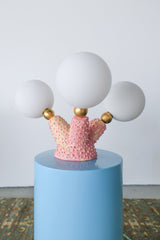 Close-up of the glossy, bumpy, bubblegum-pink glaze on this one-of-a-kind sculptural ceramic lamp, highlighting the hand-built texture, pastel pink underglaze, and 1-inch raw brass spheres that connect to glowing G9 bulbs—perfect for fans of offbeat, creature-inspired home accents and modern handmade lighting.