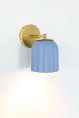 Unglazed soft blue ceramic wall sconce with solid brass hardware, featuring a scalloped silhouette that brings a charming touch to bathroom and powder room lighting; ideal for traditional, coastal, Nantucket-inspired, Southern, or transitional interiors where soft color and timeless form add a refined yet playful focal point.
