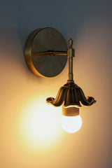 Brass floral wall sconce with cast brass detailing.  Modern take on traditional style brass light fixtures that retails old-world European charm with the finial and brass flower. Octavia wall sconce made by Sazerac Stitches in New Orleans.  Lit up with shadows.