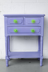 Splat drawer pull in translucent neon green acrylic with a brass detail installed on a colorful lavender dresser drawer, demonstrating its easy installation and ability to add a unique touch.