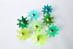 Multiple Splat drawer pulls in various finishes like greens and teals arranged on a white background, showcasing their versatility and playful character.